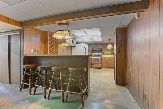 bar featuring electric range, a drop ceiling, white fridge, and wooden walls