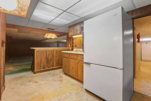 kitchen featuring wooden walls, a drop ceiling, white fridge, and hanging light fixtures