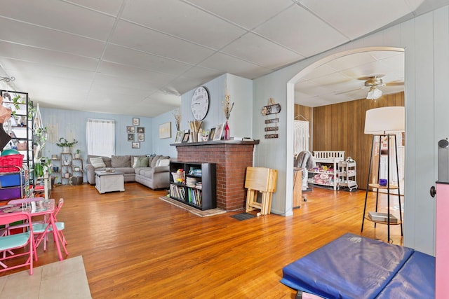 living room with hardwood / wood-style floors, a paneled ceiling, ceiling fan, and wooden walls