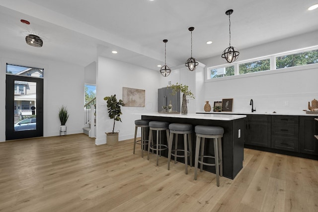 kitchen with hanging light fixtures, high end fridge, a breakfast bar, a kitchen island, and light wood-type flooring