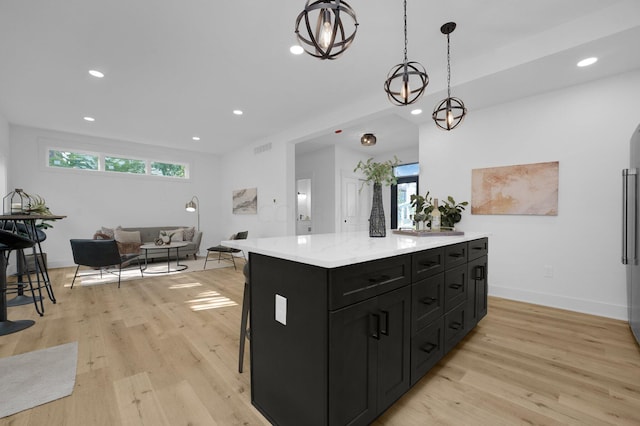 kitchen featuring pendant lighting, a center island, a kitchen breakfast bar, light hardwood / wood-style flooring, and light stone counters