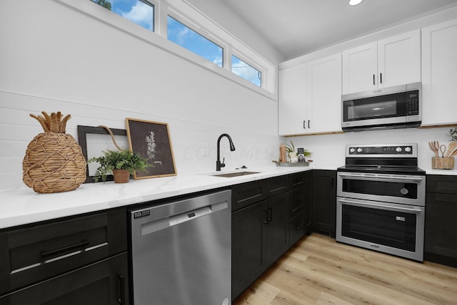 kitchen featuring sink, light hardwood / wood-style flooring, appliances with stainless steel finishes, tasteful backsplash, and white cabinetry