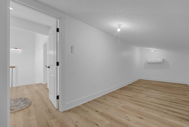 bonus room featuring a textured ceiling, light hardwood / wood-style flooring, and a wall mounted air conditioner