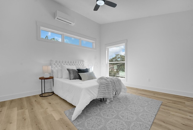 bedroom with ceiling fan, an AC wall unit, and light hardwood / wood-style flooring