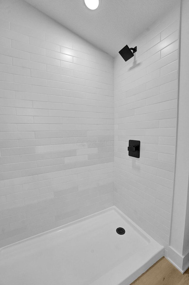 bathroom featuring wood-type flooring, a textured ceiling, and a tile shower