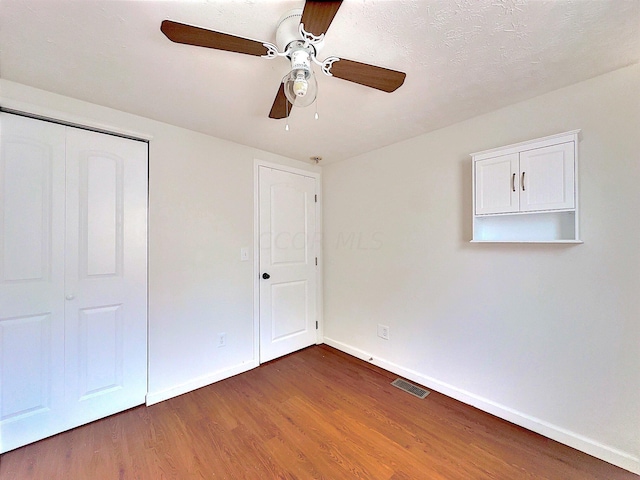 unfurnished bedroom with ceiling fan, a closet, dark wood-type flooring, and a textured ceiling