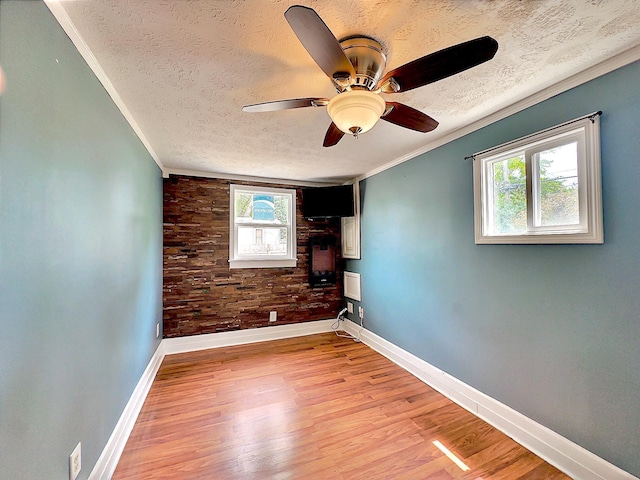 empty room with ceiling fan, ornamental molding, a textured ceiling, and light wood-type flooring