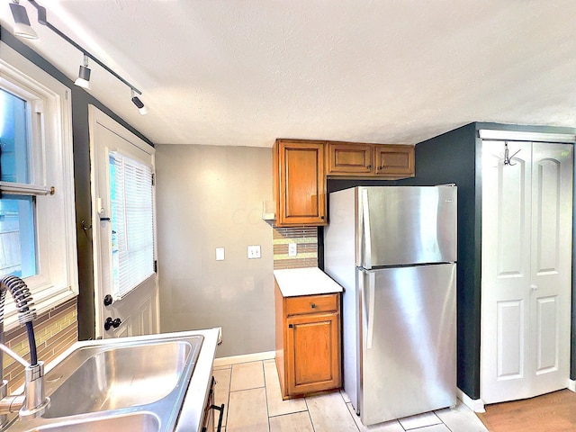 kitchen with sink, stainless steel fridge, track lighting, a textured ceiling, and decorative backsplash