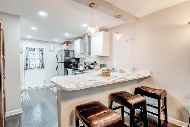 kitchen featuring white cabinetry, wall chimney range hood, kitchen peninsula, a breakfast bar area, and appliances with stainless steel finishes