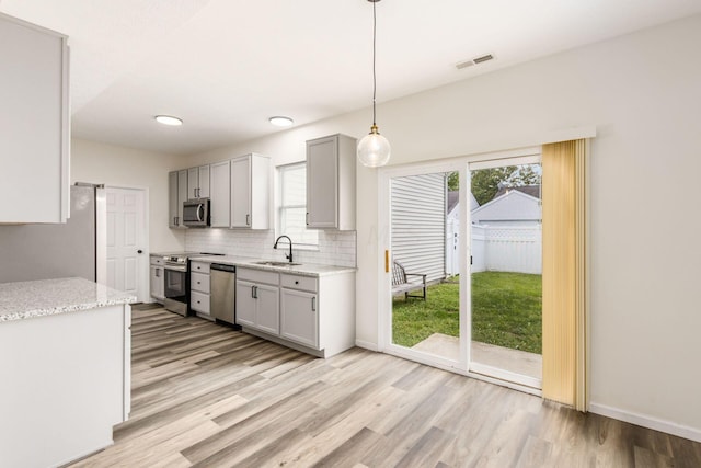 kitchen featuring light stone countertops, sink, light hardwood / wood-style flooring, decorative light fixtures, and appliances with stainless steel finishes