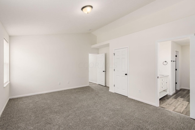 unfurnished bedroom featuring carpet flooring, a closet, vaulted ceiling, and ensuite bath