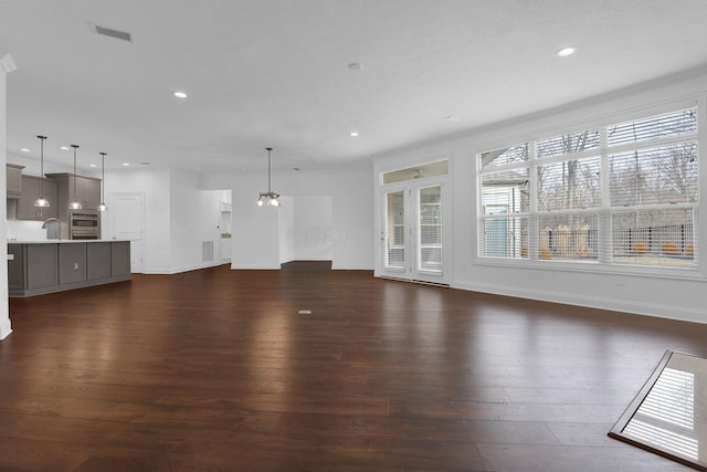 unfurnished living room featuring dark hardwood / wood-style flooring, sink, and an inviting chandelier