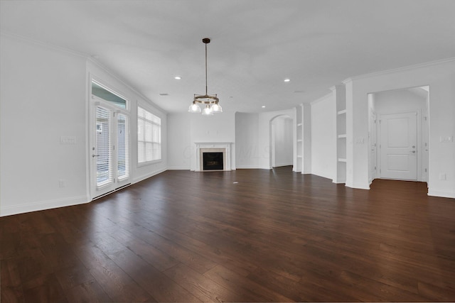 unfurnished living room with crown molding, dark wood-type flooring, an inviting chandelier, and built in shelves