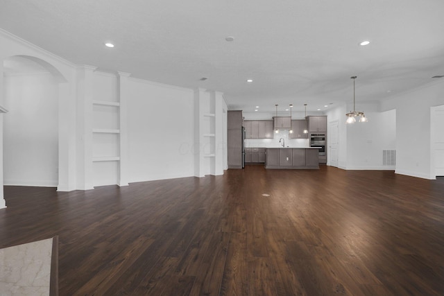 unfurnished living room with sink, crown molding, dark wood-type flooring, and a chandelier