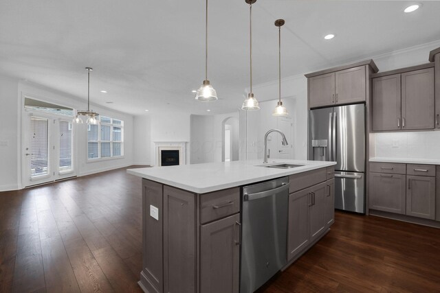 kitchen with stainless steel appliances, decorative light fixtures, sink, and a center island with sink