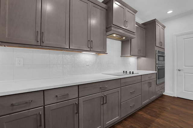 kitchen featuring tasteful backsplash, crown molding, dark hardwood / wood-style flooring, double oven, and black electric stovetop