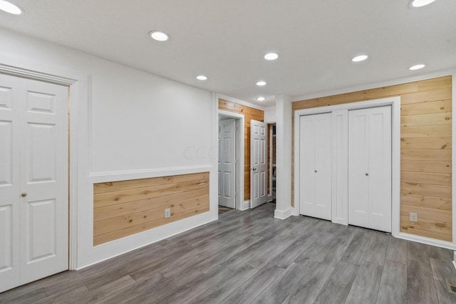 unfurnished bedroom with hardwood / wood-style flooring, multiple closets, and wood walls