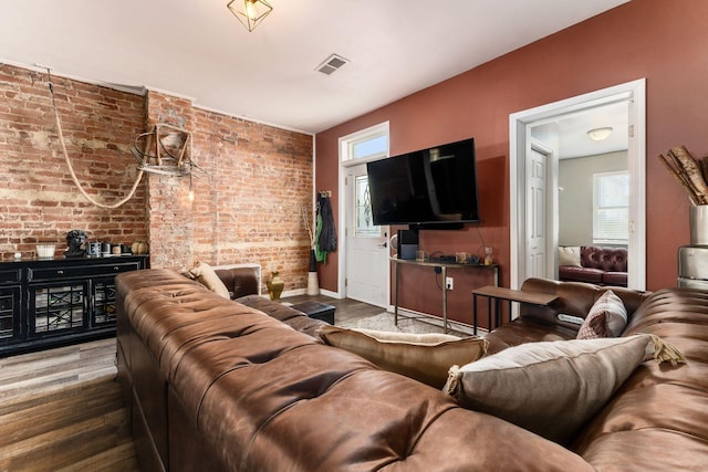 living room with hardwood / wood-style flooring, a healthy amount of sunlight, and brick wall