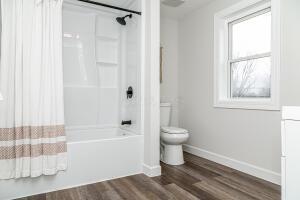 bathroom with washtub / shower combination, toilet, and wood-type flooring