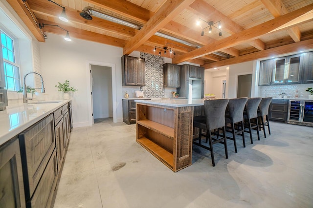 kitchen with decorative backsplash, dark brown cabinets, sink, beam ceiling, and a kitchen island