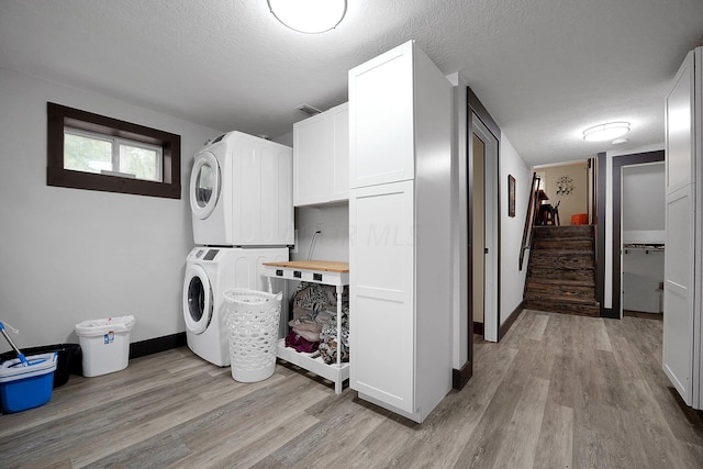 laundry room featuring cabinets, stacked washing maching and dryer, a textured ceiling, and light hardwood / wood-style floors