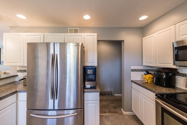 kitchen with appliances with stainless steel finishes, tasteful backsplash, dark stone counters, dark tile patterned flooring, and white cabinetry