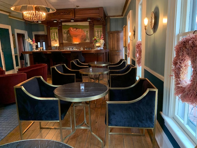 bar featuring wood-type flooring, crown molding, and an inviting chandelier