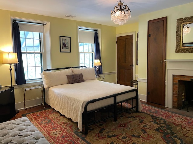 bedroom featuring a brick fireplace, a notable chandelier, dark wood-type flooring, and multiple windows