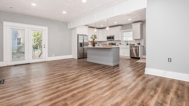 kitchen featuring a kitchen island, hardwood / wood-style floors, pendant lighting, white cabinets, and appliances with stainless steel finishes