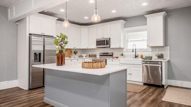 kitchen featuring appliances with stainless steel finishes, dark wood-type flooring, sink, white cabinetry, and hanging light fixtures