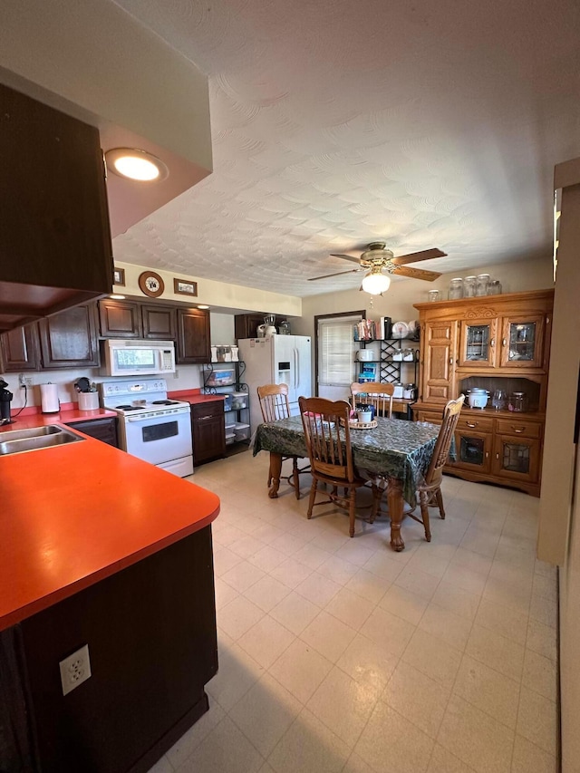 interior space with dark brown cabinetry, ceiling fan, sink, a textured ceiling, and white appliances