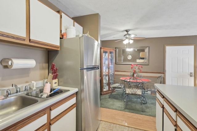 kitchen featuring stainless steel refrigerator, white cabinetry, sink, ceiling fan, and light wood-type flooring