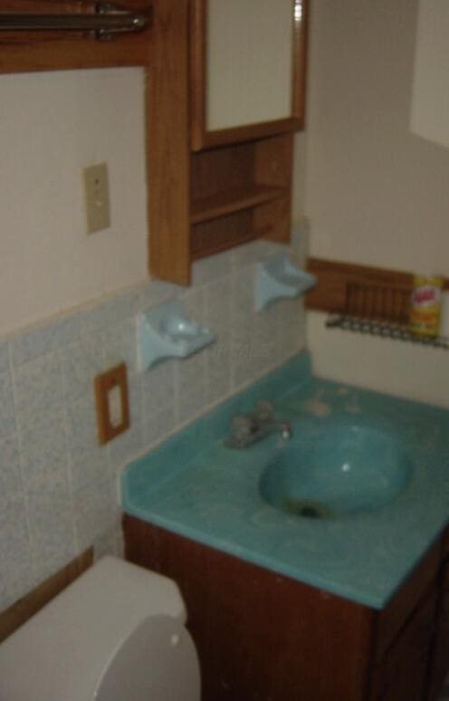 bathroom with decorative backsplash, vanity, toilet, and tile walls