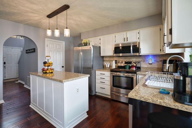 kitchen with stainless steel appliances, a center island, tasteful backsplash, white cabinets, and decorative light fixtures