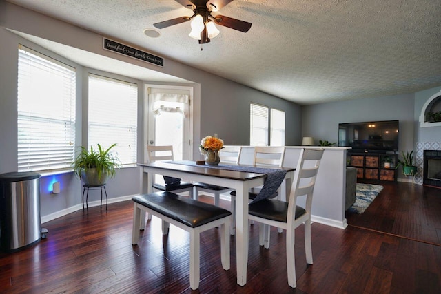 dining area with dark hardwood / wood-style flooring, ceiling fan, a fireplace, and a textured ceiling