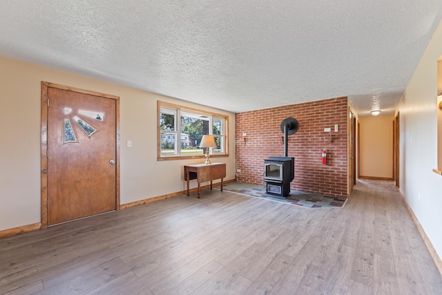 unfurnished living room with a wood stove, light hardwood / wood-style flooring, brick wall, and a textured ceiling