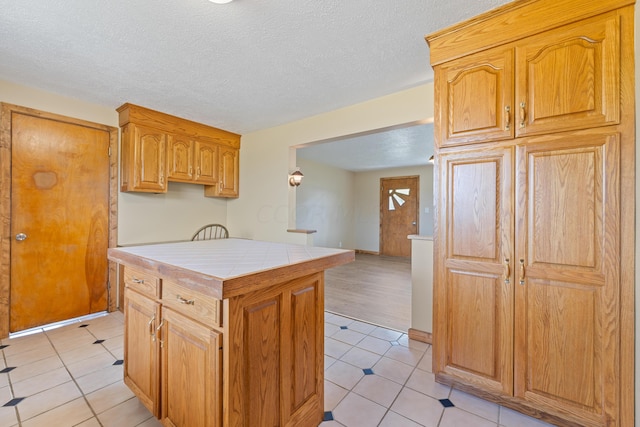 kitchen with tile countertops, a center island, light tile patterned floors, and a textured ceiling