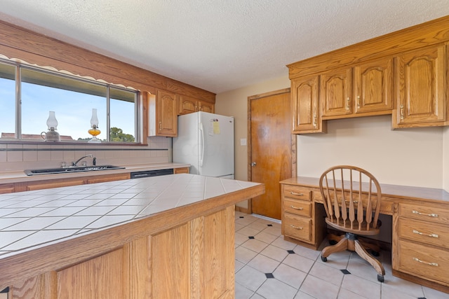 kitchen with sink, white refrigerator, backsplash, tile countertops, and built in desk