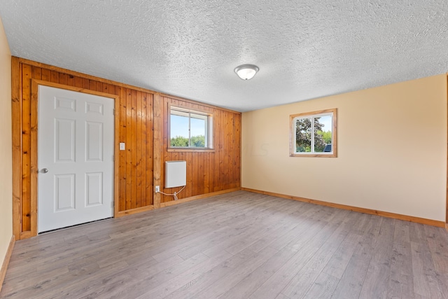 spare room with wooden walls, a textured ceiling, and light wood-type flooring