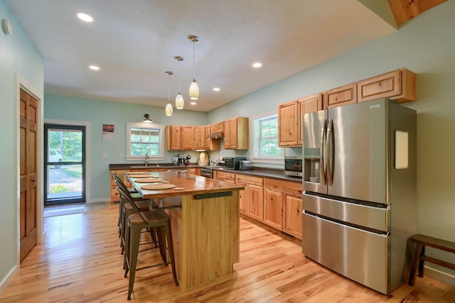 kitchen with decorative light fixtures, a kitchen island, stainless steel appliances, and a wealth of natural light