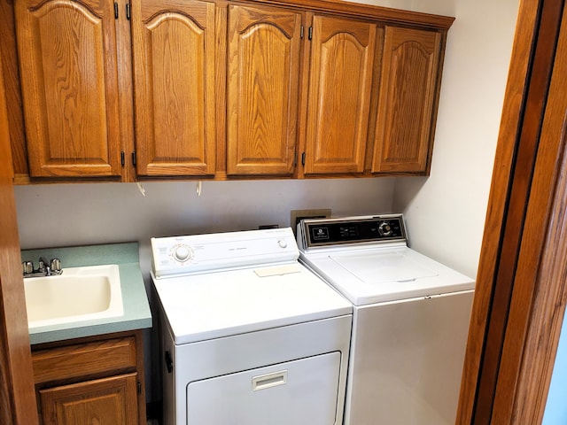 clothes washing area featuring washing machine and clothes dryer, sink, and cabinets