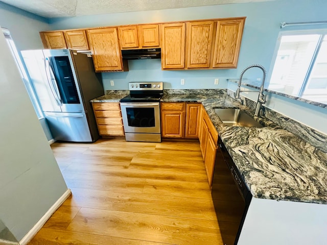 kitchen with sink, stainless steel appliances, dark stone countertops, extractor fan, and light hardwood / wood-style floors