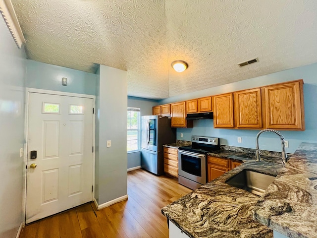 kitchen featuring sink, stainless steel appliances, dark stone countertops, a textured ceiling, and light wood-type flooring