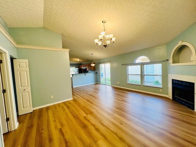 unfurnished living room with hardwood / wood-style floors, lofted ceiling, a tile fireplace, a textured ceiling, and a notable chandelier