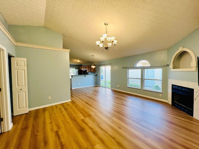 unfurnished living room featuring hardwood / wood-style floors, a textured ceiling, a tile fireplace, and vaulted ceiling