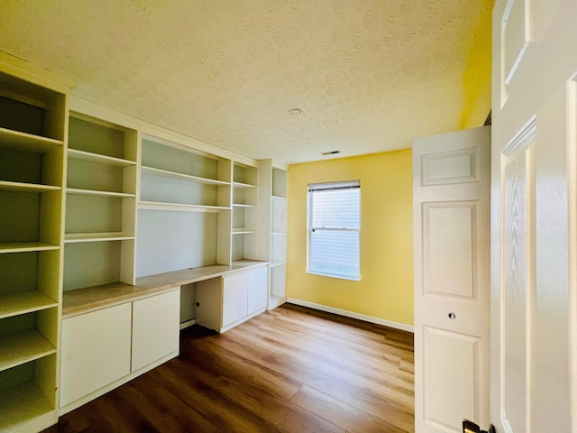 unfurnished office featuring built in desk, a textured ceiling, and wood-type flooring