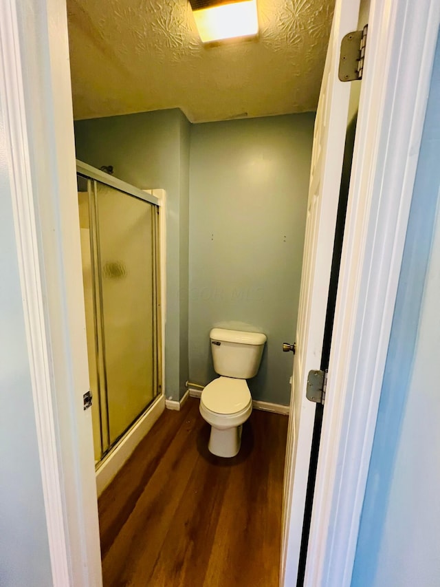 bathroom featuring a shower with shower door, toilet, wood-type flooring, and a textured ceiling