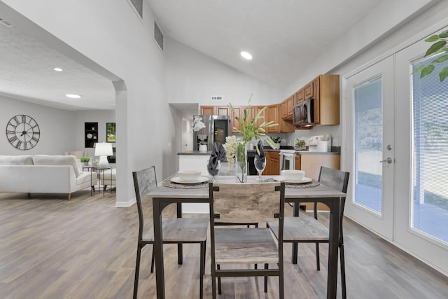 dining area featuring light wood-type flooring, high vaulted ceiling, and french doors