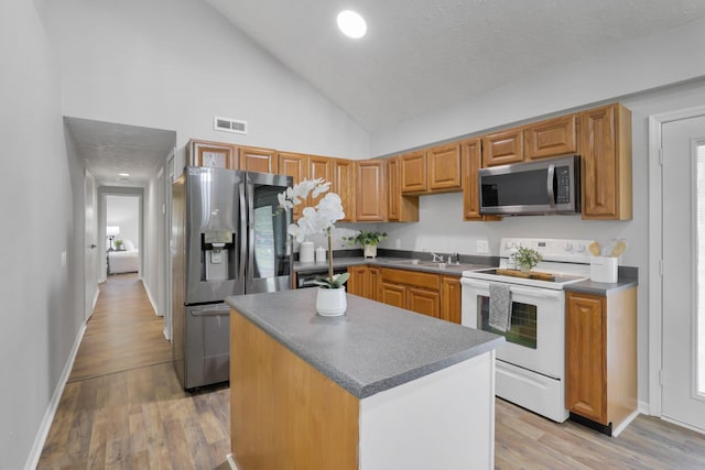 kitchen with sink, a center island, stainless steel appliances, light hardwood / wood-style flooring, and high vaulted ceiling