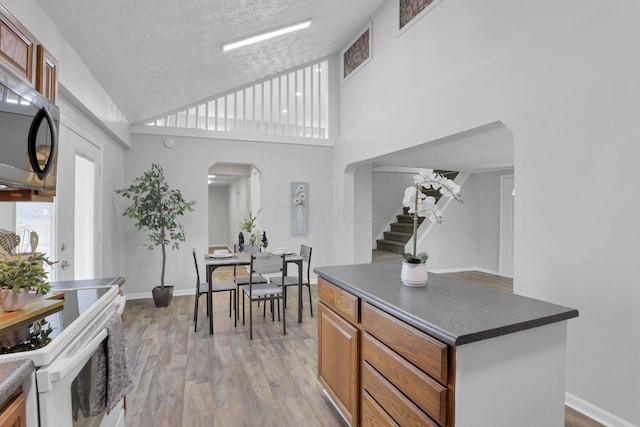 kitchen featuring white range with electric stovetop, light wood-type flooring, a textured ceiling, and a towering ceiling